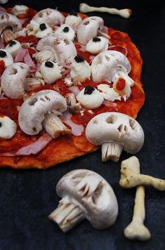 a pizza with mushrooms and other toppings sitting on top of a black surface next to bone bones