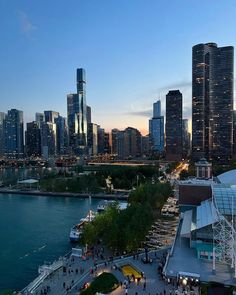 the city skyline is lit up at night with people walking on the sidewalk and in the water