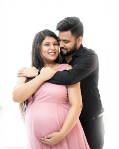 a pregnant woman hugging her husband for the camera