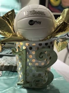 a white ball sitting on top of a table next to a cup with gold foil