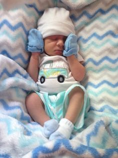 a baby laying on top of a blanket wearing a blue and white hat with a vw bus on it