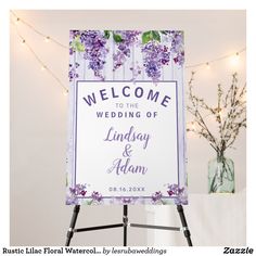 a welcome sign with purple flowers and greenery in the background is displayed on an easel