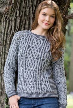 a woman standing next to a tree wearing a sweater