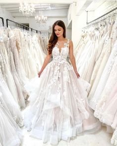 a woman is standing in front of some wedding gowns and looking at the camera