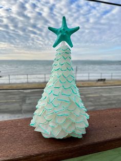 a ceramic christmas tree sitting on top of a wooden table next to the ocean and sky