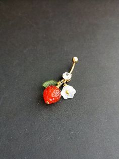 a red strawberry and white flower dangling from a gold navel ring on a black surface