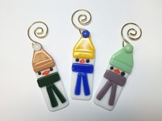 three glass keychains with snowmen on them, one wearing a hat and the other holding a scarf