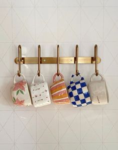 three mugs are hanging on the wall with brass hooks and hangers in front of them