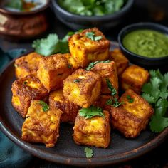 a plate full of tofu cubes with cilantro and green sauce on the side