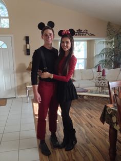 a man and woman in mickey mouse ears standing next to each other on a wooden floor