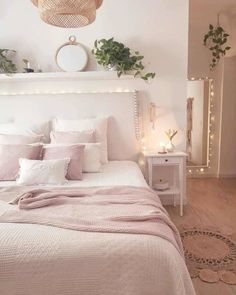 a white bed topped with lots of pillows and blankets next to a night stand filled with plants