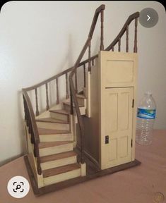 a dollhouse staircase made out of an old door and wooden handrails with a water bottle on the side