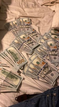 a pile of money sitting on top of a bed next to a pair of jeans