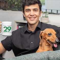 a man sitting on a couch holding a coffee mug with his dog