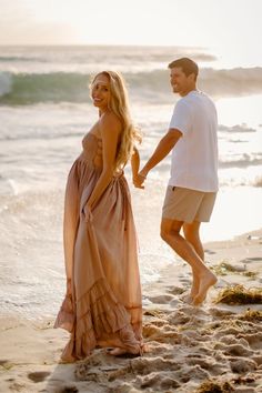 a man and woman walking on the beach holding hands