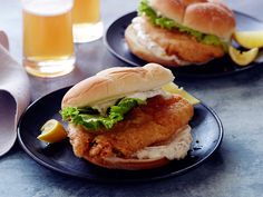 two fish sandwiches on black plates with lemon wedges and beer in the back ground