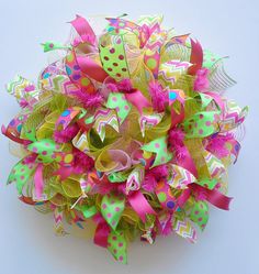 a close up of a colorful wreath on a white surface with pink, green and yellow decorations