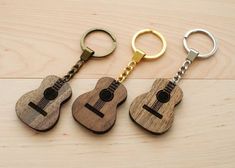 three wooden guitar shaped key chains are on a table with two keys in the shape of an ukulele