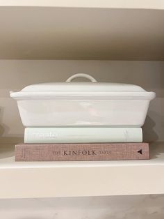 two books are stacked on top of each other in front of a white casserole dish