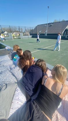 some people are sitting on a blanket at a tennis court