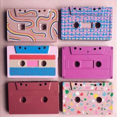 four different colored cassettes are arranged on a white surface, one is pink and the other is blue