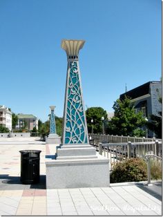 there is a blue and white clock tower in the middle of this square with a trash can next to it