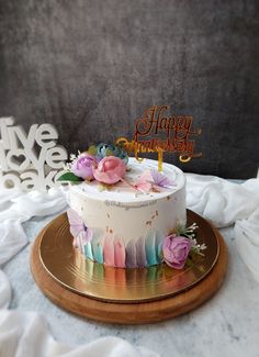 a birthday cake decorated with flowers and a happy birthday sign on top is sitting on a gold plate