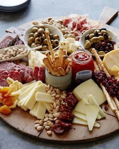 an assortment of cheeses, meats and nuts on a wooden platter with olives