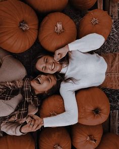 two women standing in front of pumpkins on the ground with their arms around each other