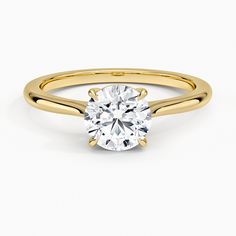 a yellow gold engagement ring with a round cut diamond in the center, on a white background