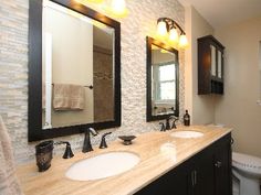 a bathroom with two sinks, mirrors and lights on the wall next to the toilet