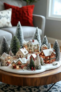 a christmas village on a coffee table in front of a couch with red and white pillows