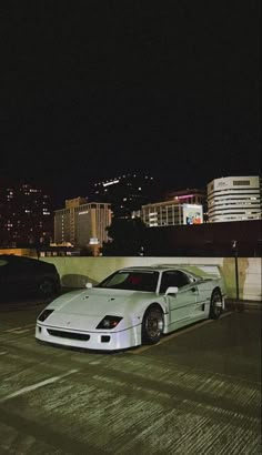 a white sports car parked in an empty parking lot next to some tall buildings at night