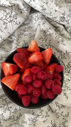 strawberries and raspberries in a black bowl on a white floral print tablecloth