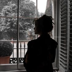 a woman standing in front of a window next to a potted plant