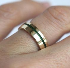 a close up of a person's hand wearing a gold ring with green stripes