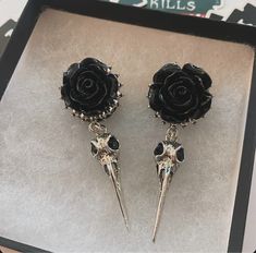 two black roses with spikes on them are in a box next to a pair of earrings