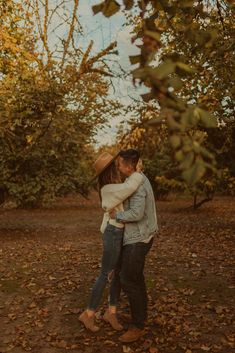 a man and woman hugging in the woods with leaves on the ground around them,