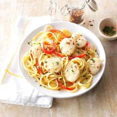 a white bowl filled with pasta and shrimp on top of a wooden table next to a cup