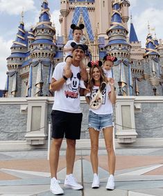 three people standing in front of a castle with mickey mouse ears on their heads and one person wearing minnie mouse ears