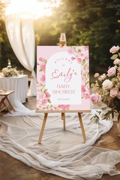 a baby shower sign sitting on top of a wooden easel next to pink flowers