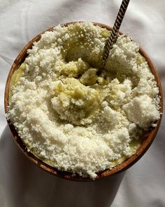 a wooden bowl filled with food on top of a white cloth covered table next to a metal spoon