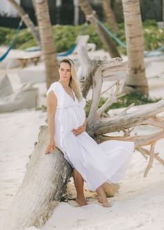 a pregnant woman sitting on top of a wooden log in the sand next to palm trees