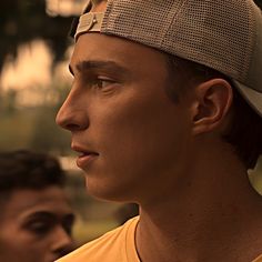 a close up of a person wearing a hat and looking off into the distance with trees in the background