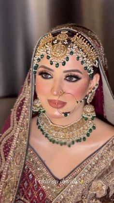 a woman in a bridal outfit with jewelry on her face and nose is wearing an elaborate head piece