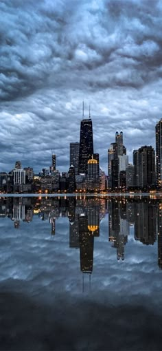 a city skyline is reflected in the water at night with dark clouds and blue sky