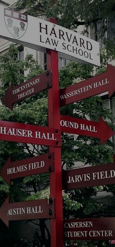 a red and white street sign with many different signs on it's sides in front of a building