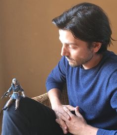 a man sitting in a chair next to a figurine on his lap and looking down