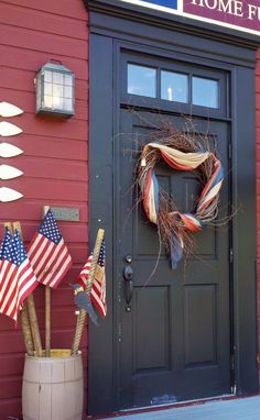 an american flag wreath is on the front door of a red building with patriotic flags