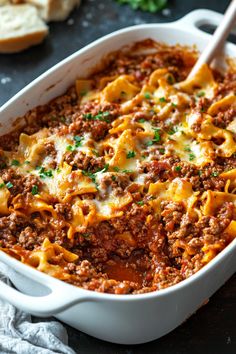 a casserole dish with meat and cheese in it, on a table next to bread